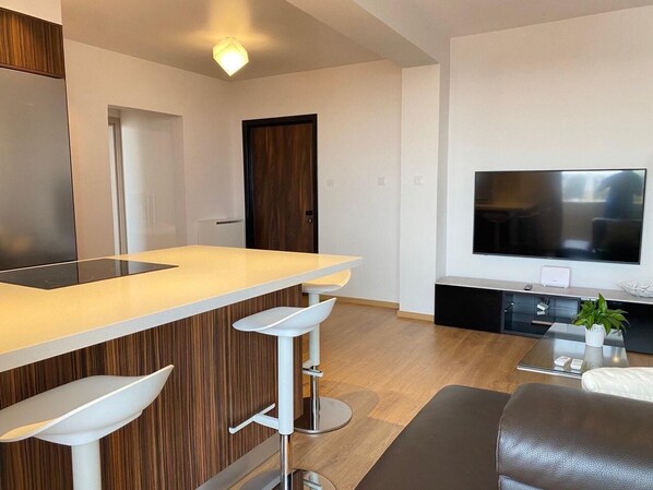 Una cocina moderna con barra, televisor grande y comedor con sofá y planta.