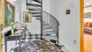 Eine Treppe mit schwarz-weiß kariertem Boden, ein Schreibtisch mit einer Vase und einer Lampe sowie ein Gemälde an der Wand.