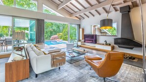 Una sala moderna con un ventanal grande, chimenea y vista a la piscina.