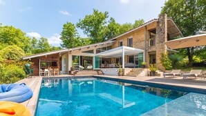 Una casa moderna con piscina, mobiliario exterior y un porche cubierto.