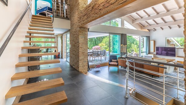 Un interior moderno con una escalera de madera, un pilar de piedra y vistas al exterior.