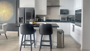 A modern kitchen with white cabinets, stainless steel appliances, and a central island with two black bar stools.