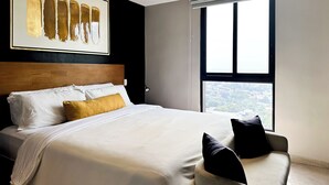 A modern hotel room with a large bed, a view of the city through a large window, and a framed artwork on the wall.