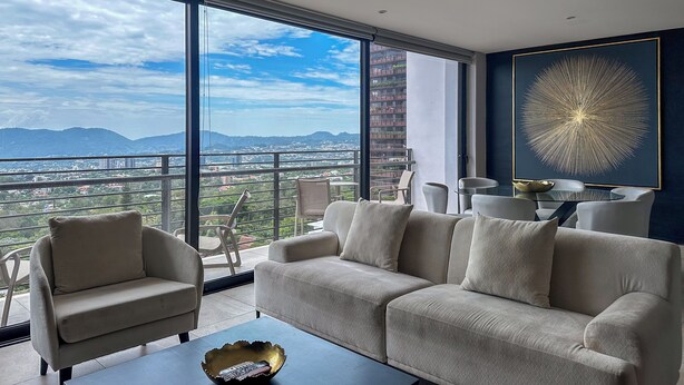 A modern living room with a large window, a sofa, a coffee table, and a dining area with chairs and a table.