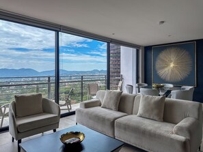 A modern living room with a large window, a sofa, a coffee table, and a dining area with chairs and a table.