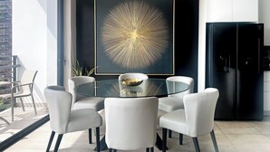 A modern kitchen with a black refrigerator, a glass table surrounded by white chairs, and a large abstract gold artwork on the wall.