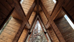 An attic bedroom with a sloped ceiling, wooden beams, and a bed with pillows and a striped pillow. - Modern A-Frame • Forest Views + Hot Tub • 30 min to Yellowstone (Island Park)