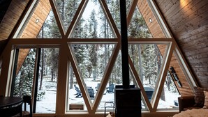 A cozy attic room with a large triangular window, wooden beams, and a fireplace. - Modern A-Frame • Forest Views + Hot Tub • 30 min to Yellowstone (Island Park)