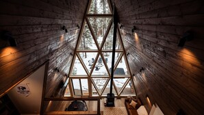 A cozy cabin with a wooden interior, a large triangular window, and a view of a snowy landscape. - Modern A-Frame • Forest Views + Hot Tub • 30 min to Yellowstone (Island Park)
