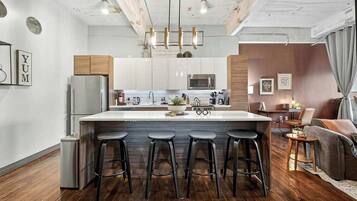 Una cocina moderna con una isla central, taburetes de bar, electrodomésticos de acero inoxidable y techo de madera.