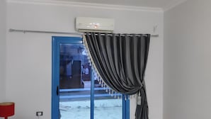 Een kamer met een deur met blauwe lijst, een wandairconditioner, een zwart gordijn, een rode lamp en een aan de muur bevestigde televisie.