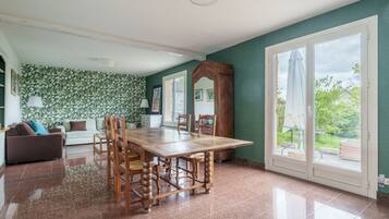 A spacious room with a wooden dining table, a sofa, and a large window with a view of greenery.