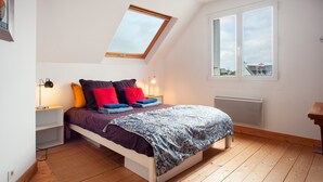 Un dormitorio con tragaluces, una cama con ropa de cama colorida, una mesita de noche con lámpara y vistas a través de una ventana.