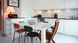 Una cocina moderna con armarios blancos, una mesa de comedor con sillas, una cafetera y un cuadro enmarcado en la pared.