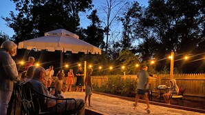 An outdoor seating area with tables and chairs, surrounded by a wooden fence and trees. - Spacious Historical 6-bed house in Princeton. Pool, bocce and basketball court. (Princeton)