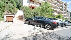 A multi-story residential building with balconies, parked cars, and a clear sky.
