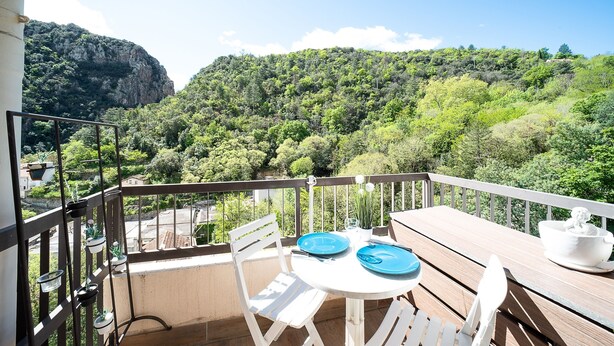 A balcony with a table, chairs, and a view of a forested hillside.
