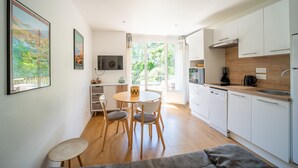 A modern kitchen with white cabinets, a dining area with a round table and chairs, and a large window providing natural light.