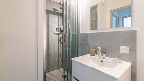 Un baño moderno con ducha de vidrio, un lavamanos blanco y un espejo encima.