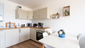 Una cocina moderna con armarios blancos, encimera de madera, microondas, cafetera y una mesa de comedor con sillas.