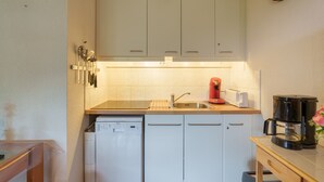 Een kleine keuken met witte kastjes, een vaatwasser, een koffiezetapparaat en een spoelbak.