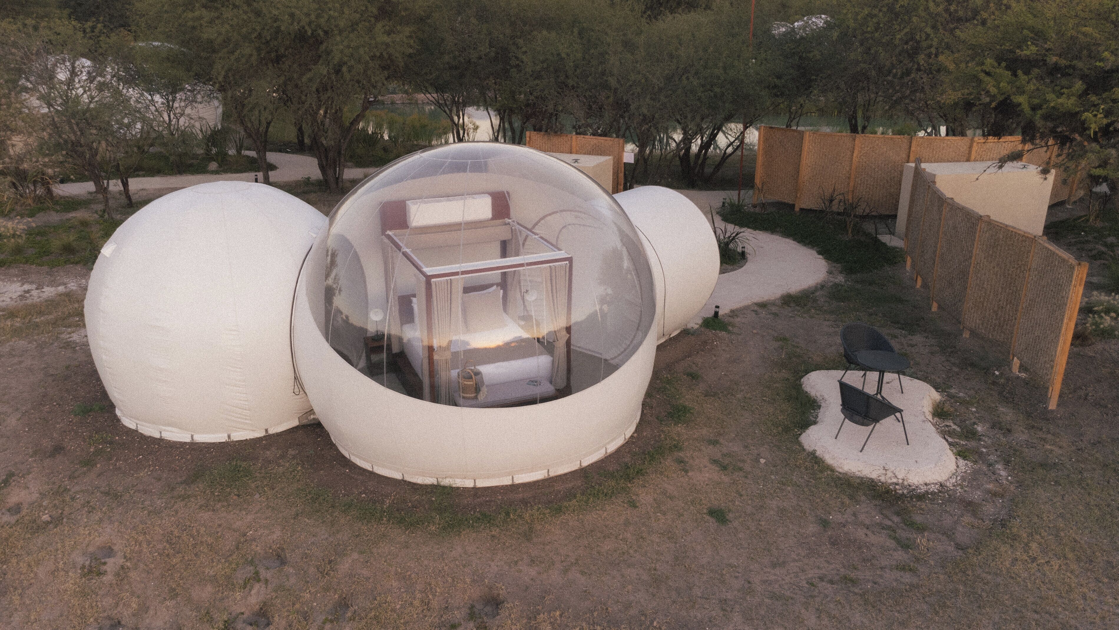 Three spherical structures with transparent walls, a small table, and a chair outside.