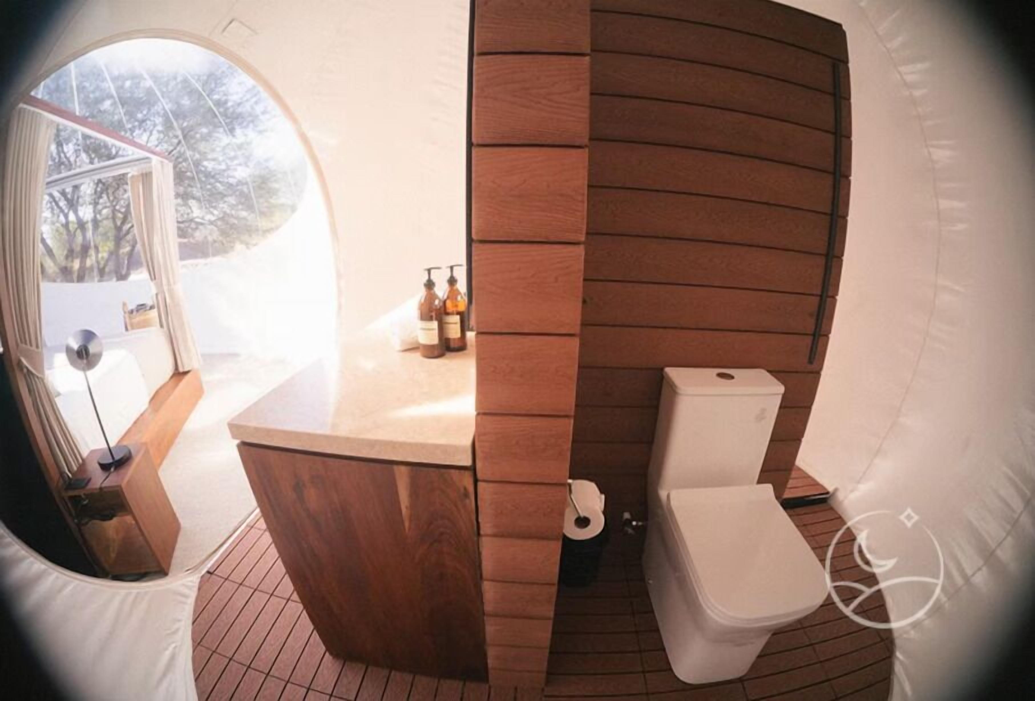 A compact bathroom with a wooden vanity, a toilet, and a small window.