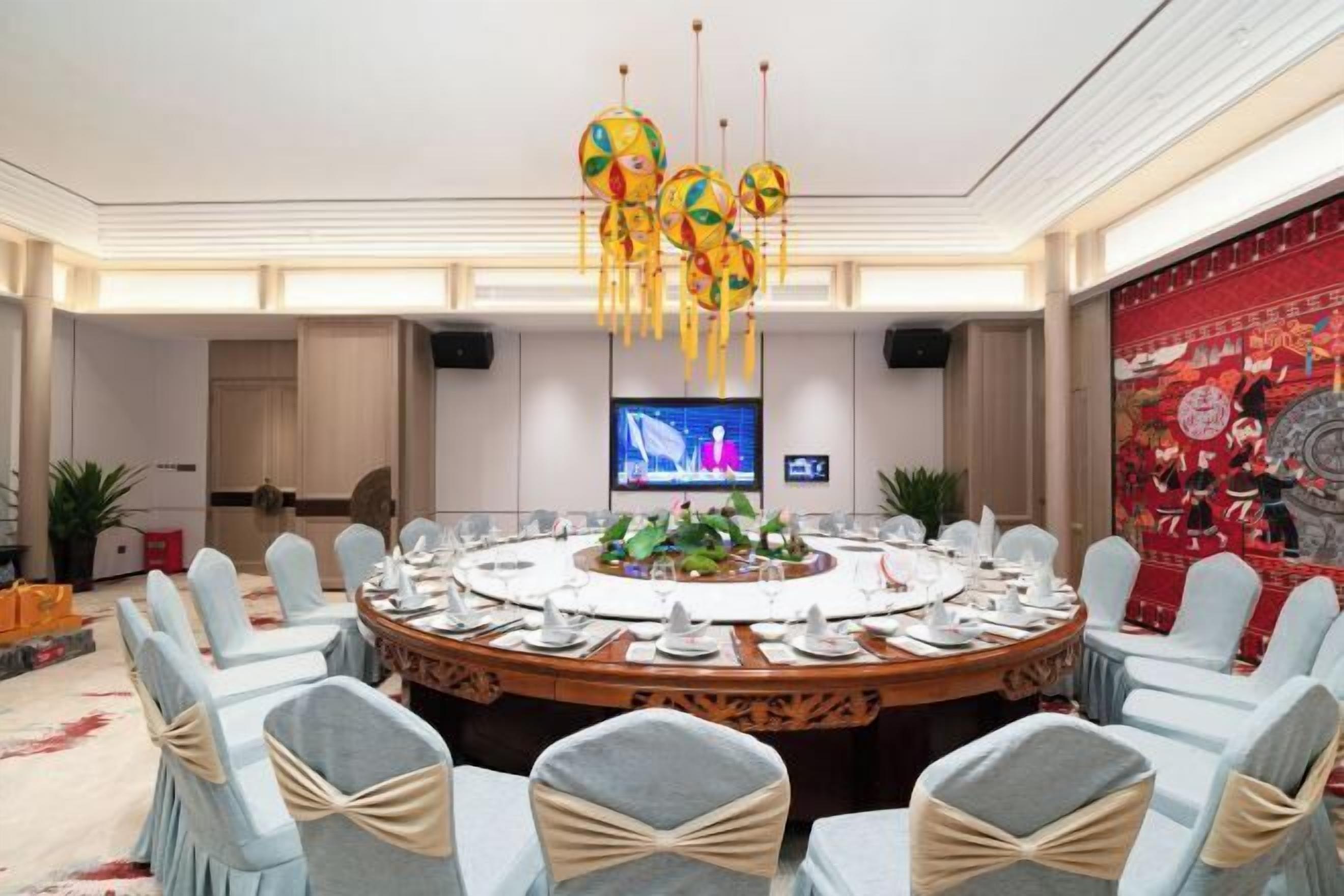 Une salle de conférence avec une table ronde, des chaises bleu clair et un lustre coloré.