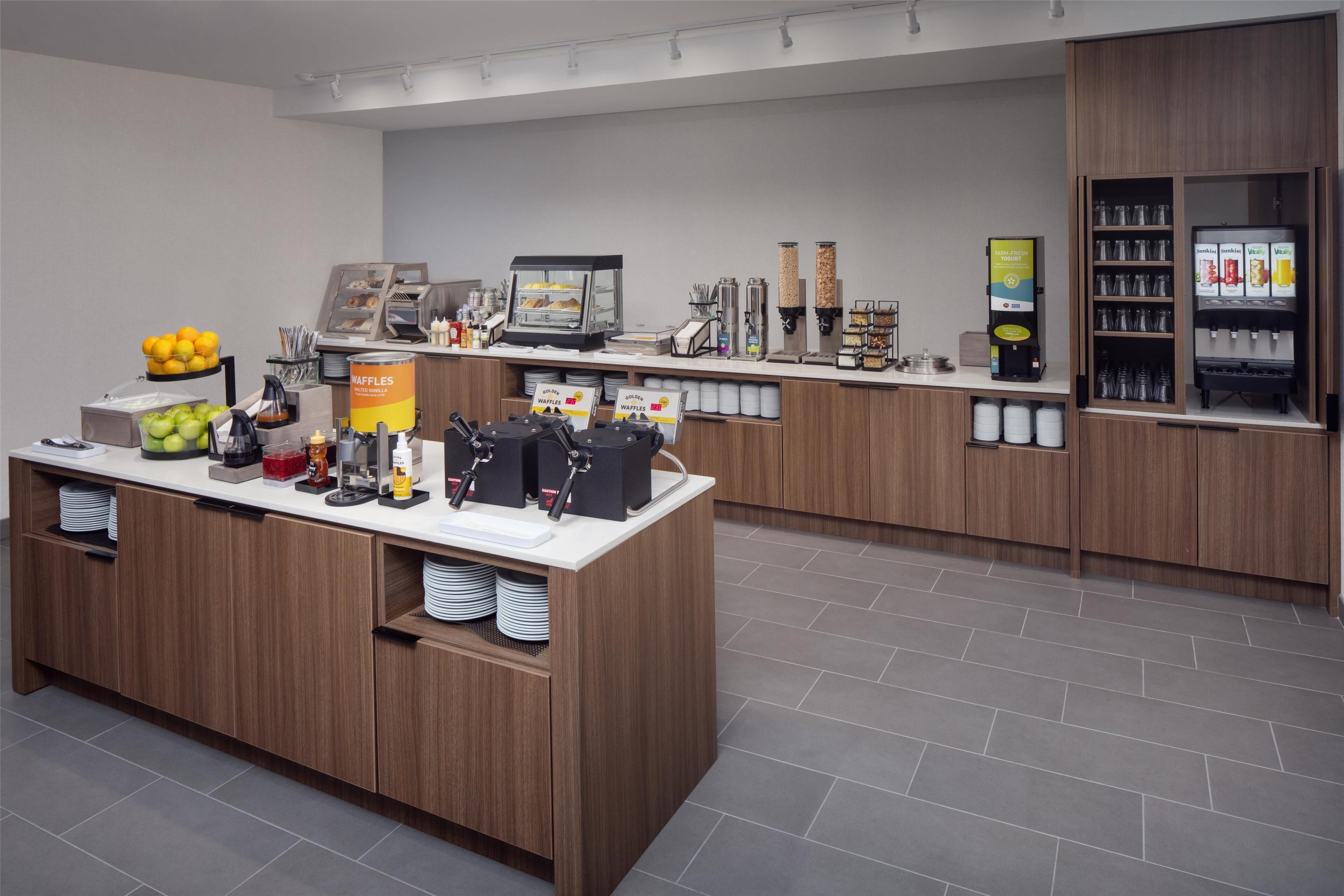 A modern breakfast bar with a coffee machine, waffle station, and fruit display.