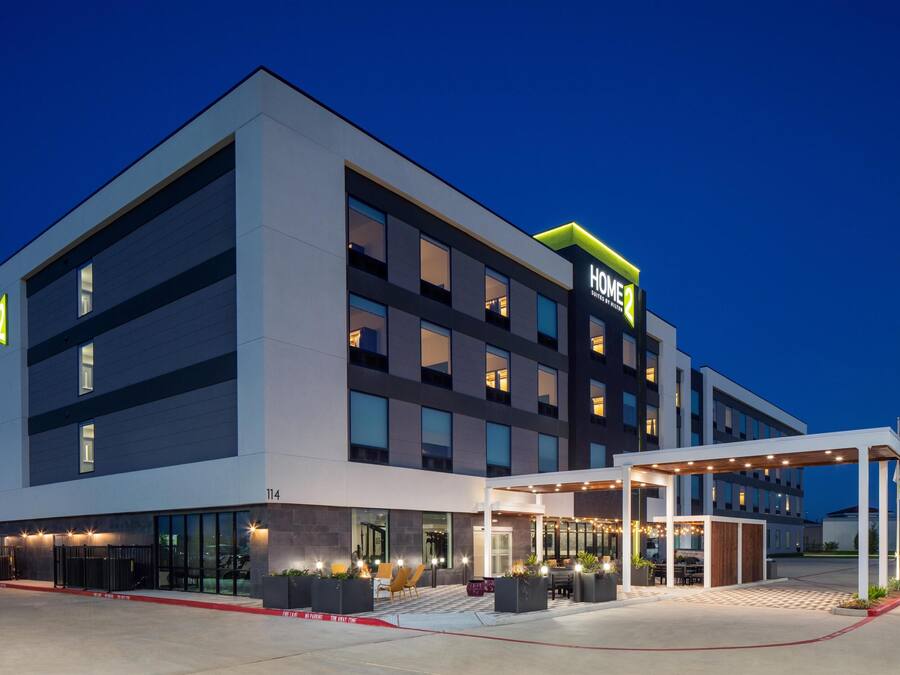 A modern hotel with a two-story structure, large windows, and a covered outdoor area with seating.