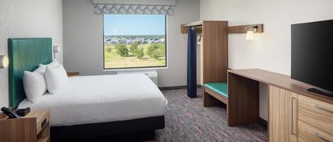 Habitación de hotel con cama, escritorio, televisión y ventana con vistas a edificios.