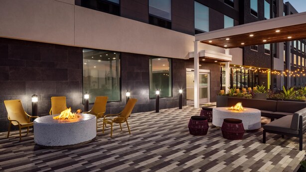 An outdoor patio area with round seating and fire pits, surrounded by modern buildings. - Home2 Suites By Hilton Bastrop, Tx (Bastrop)
