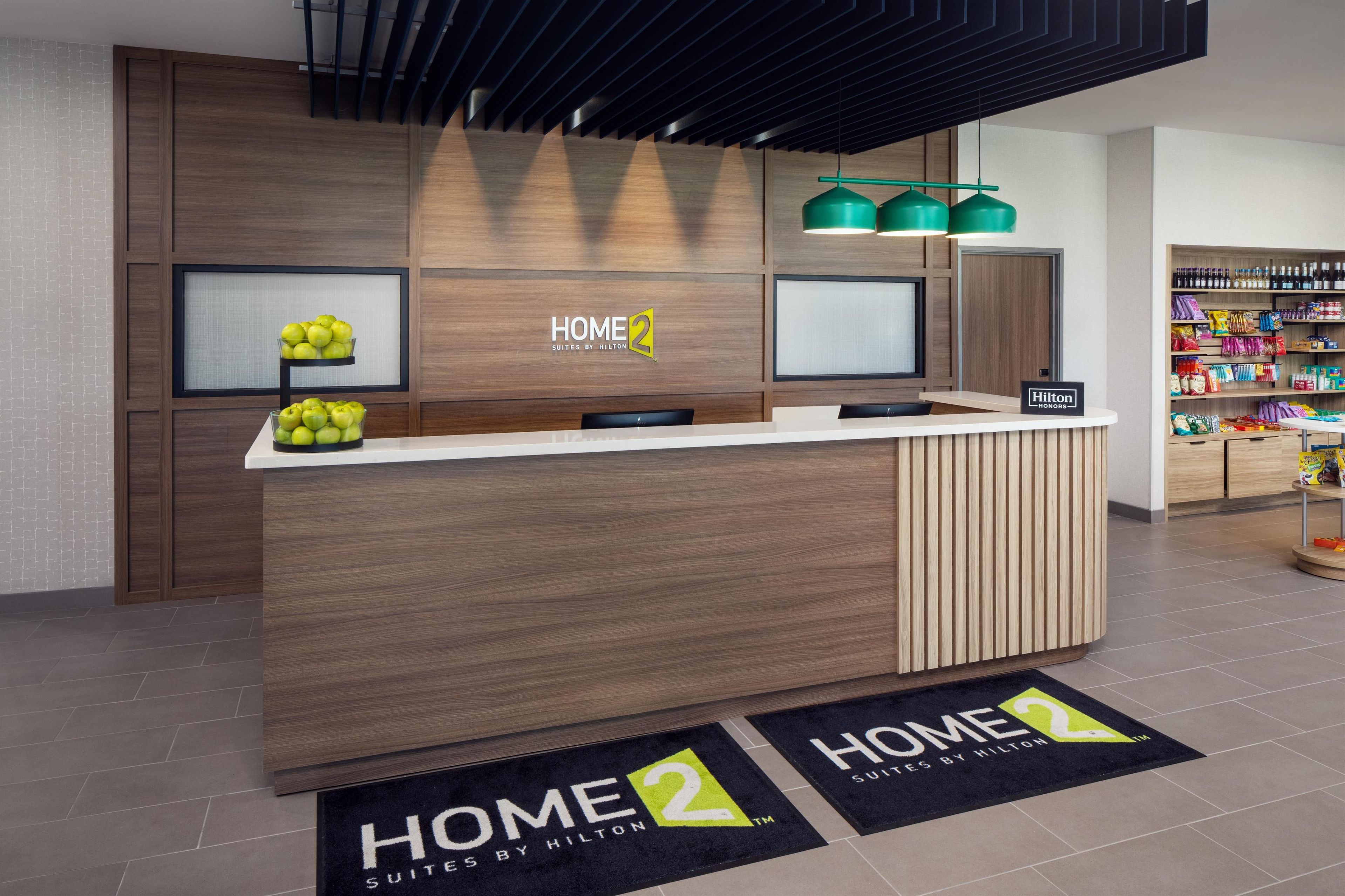 A modern hotel reception area with a wooden reception desk, a fruit display, and a minibar.