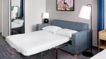 A hotel room with a single bed, a nightstand, a lamp, and a wall-mounted clock.