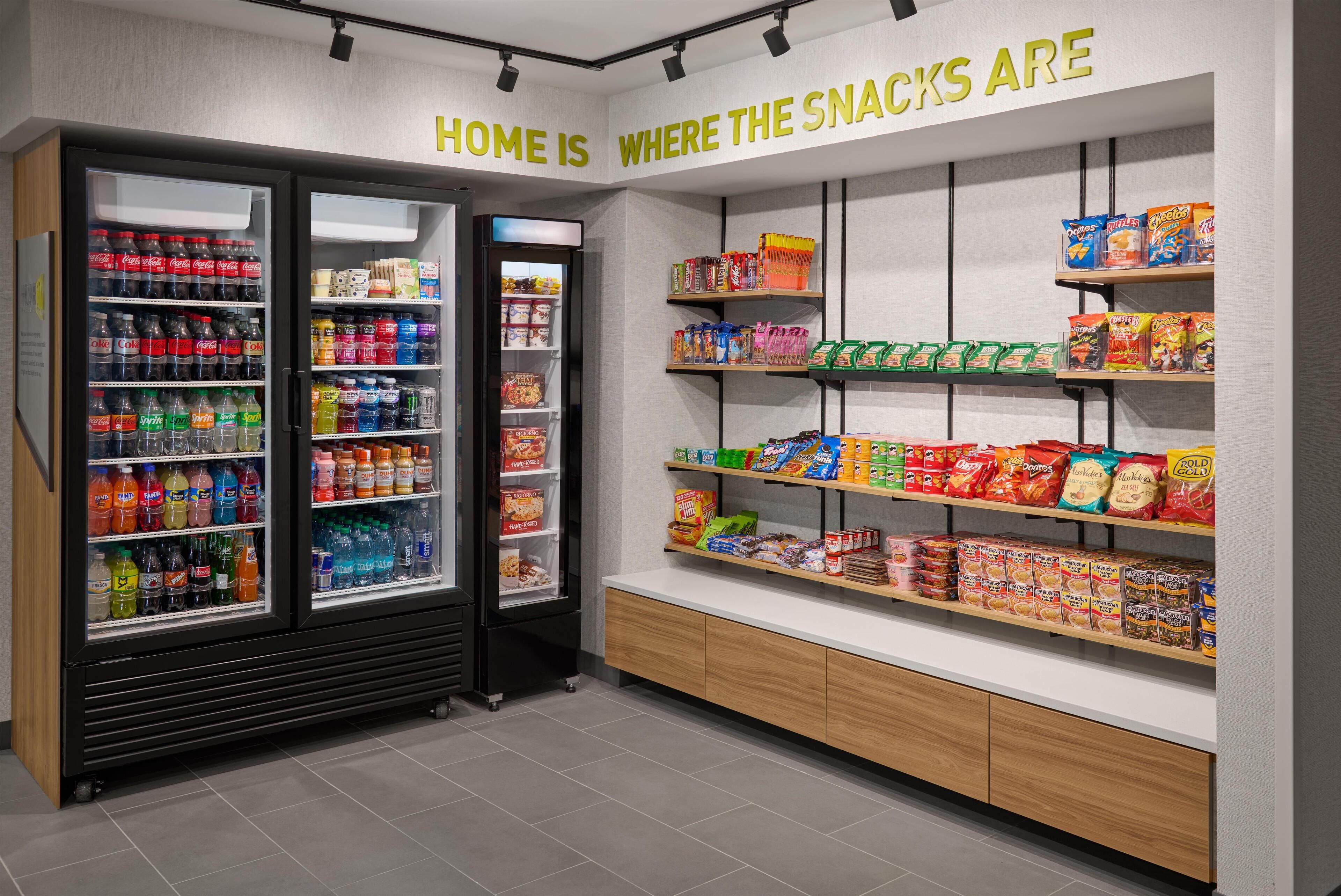 A snack section in a store with shelves stocked with various snacks and a refrigerator with beverages.
