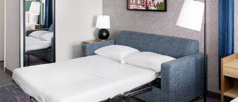 Habitación de hotel ordenada con una cama individual, una mesita de noche con lámpara, un cuadro colgado en la pared y una alfombra estampada.