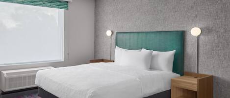 A hotel room with a bed, bedside tables, a window with blinds, and a wall with a textured pattern.