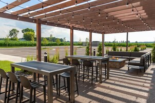 Un patio al aire libre con mesas y sillas, un hogar para fogata y vista a un campo de maíz.