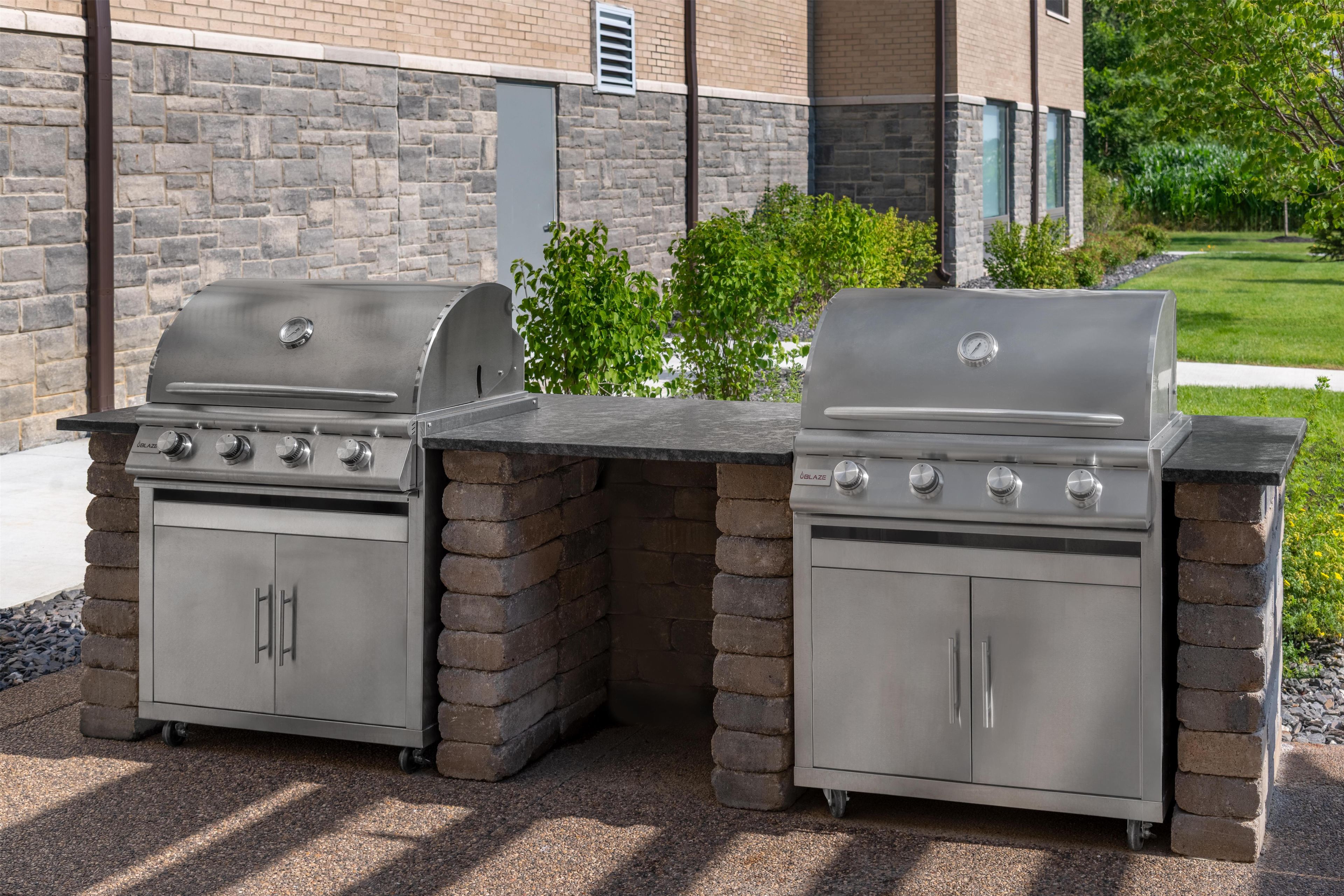 Un espace barbecue extérieur doté de deux plaques de cuisson à gaz, d’une base en briques et d’un mur en pierres en arrière-plan.