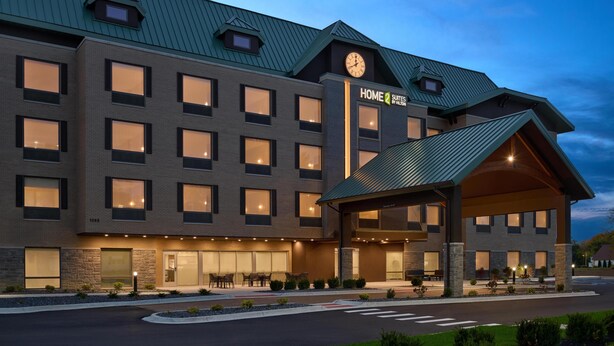Un hotel de varios pisos con diseño moderno, que presenta un área de entrada cubierta y una fachada bien iluminada.