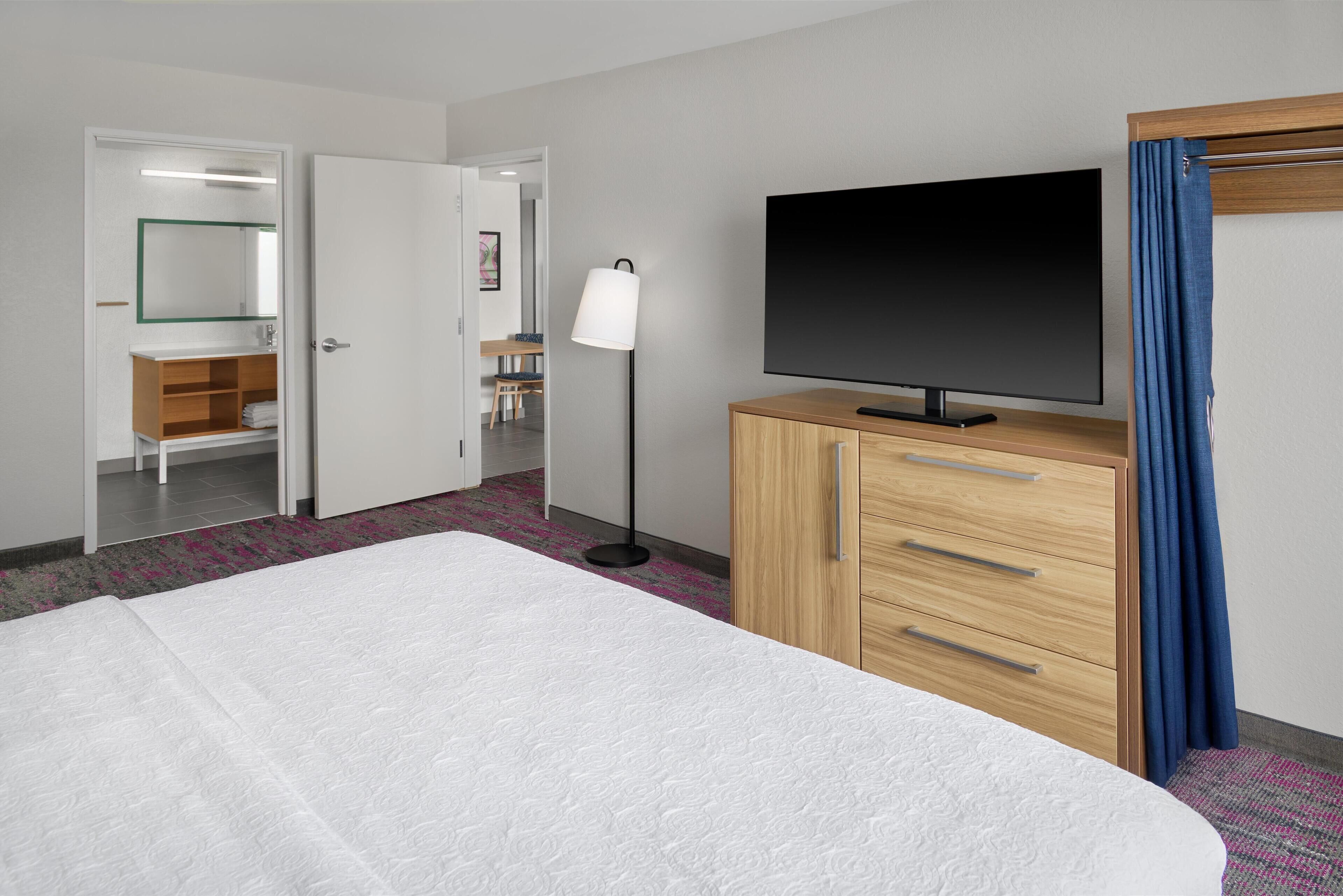 A hotel room with a bed, a TV, a wardrobe, and a bathroom visible through an open door.