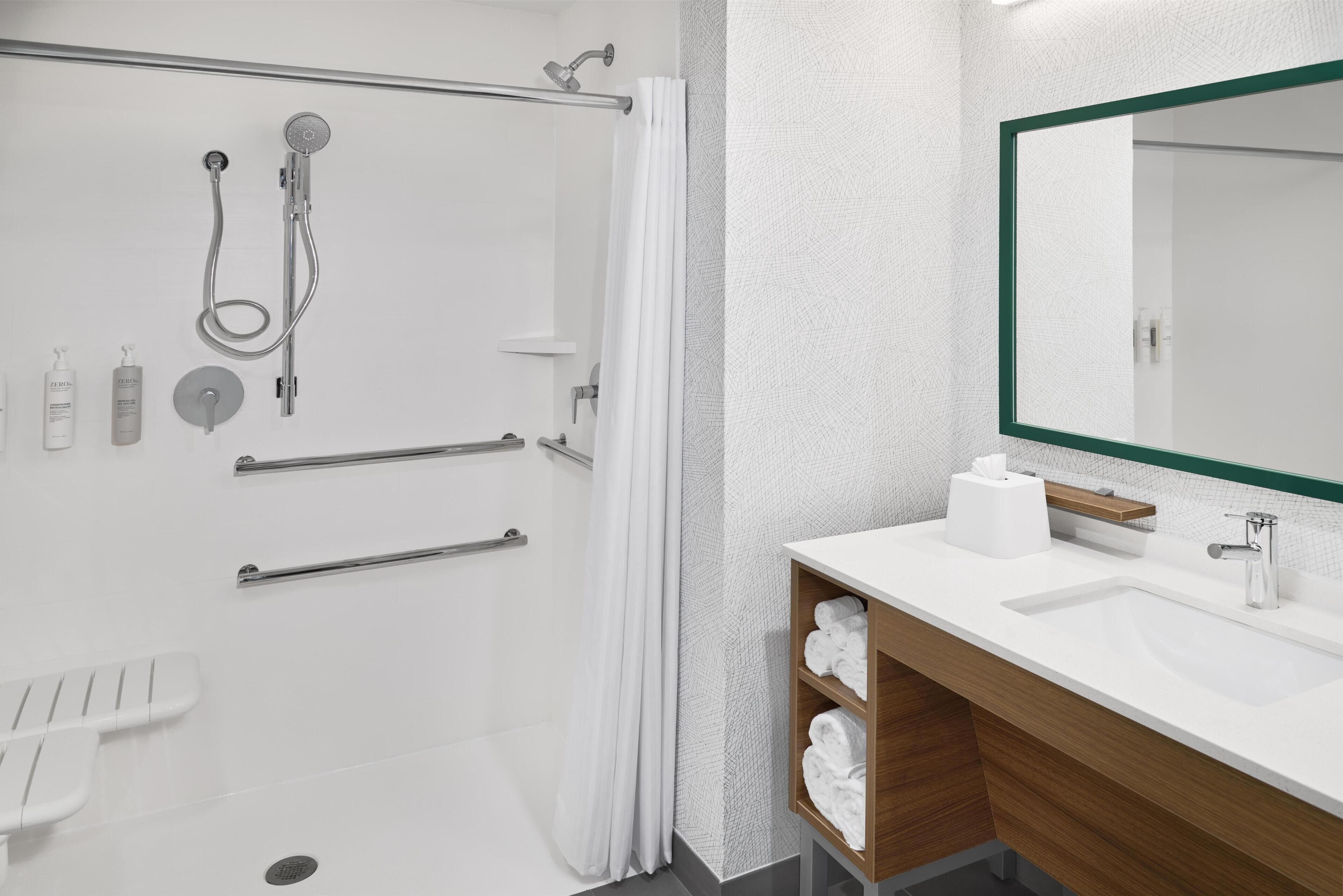 Un baño moderno con cabina de ducha, un espejo grande, un lavamanos y un perchero para toallas.