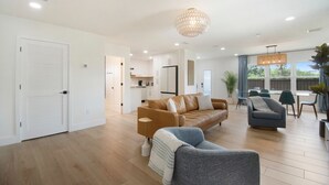A modern living room with a brown leather sofa, a grey armchair, and a dining area with blue chairs.