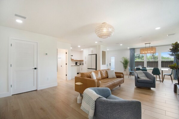 A modern living room with a brown leather sofa, a grey armchair, and a dining area with blue chairs.