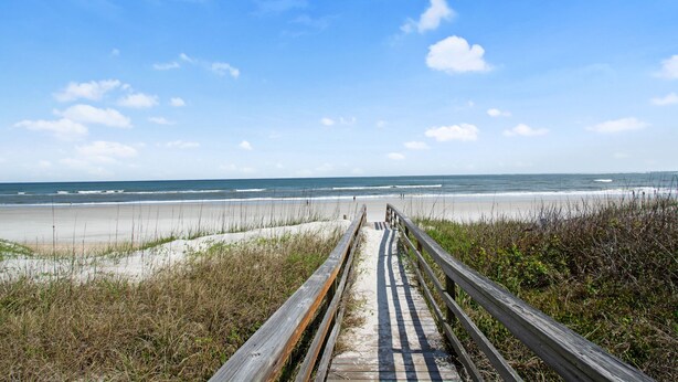 A wooden boardwalk leading to a beach with sand and waves.