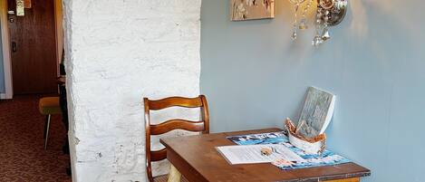 Un comedor con una mesa y sillas de madera rústica, una lámpara fijada a la pared y una puerta al fondo.