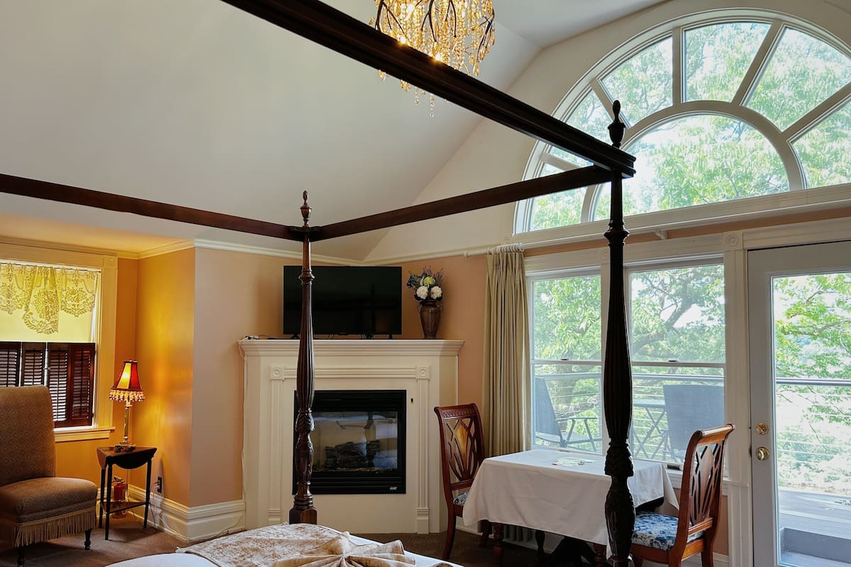 A four-poster bed, a fireplace, a television, and a dining area with chairs and a table.