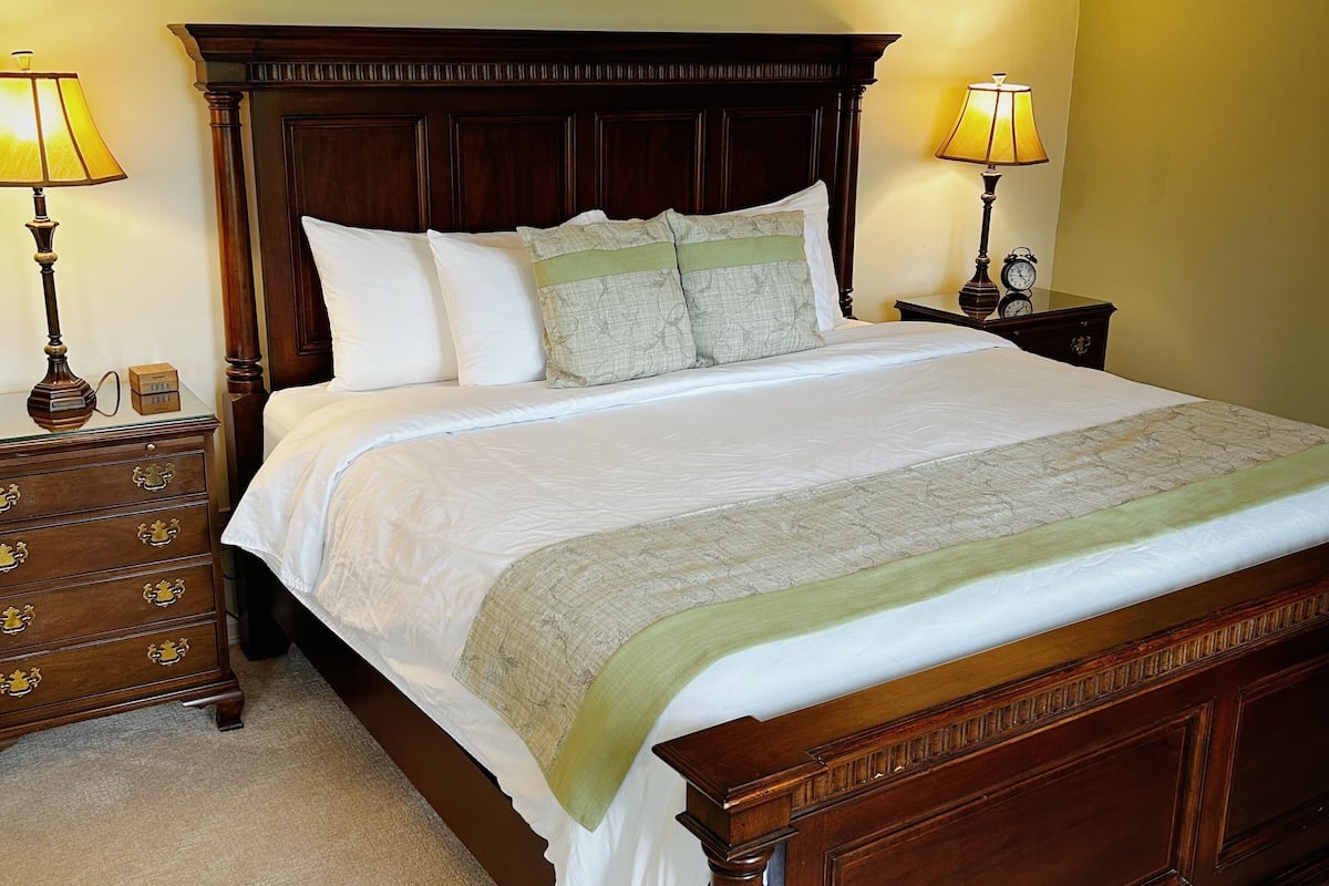 A neatly made bed with a wooden headboard, two bedside tables with lamps, and a carpeted floor.