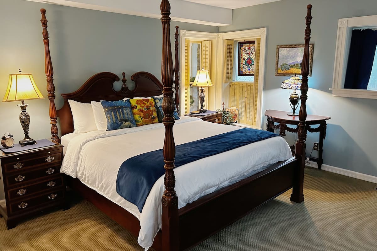 A four-poster bed with a wooden headboard, a bedside table with a lamp, and a nightstand with drawers.