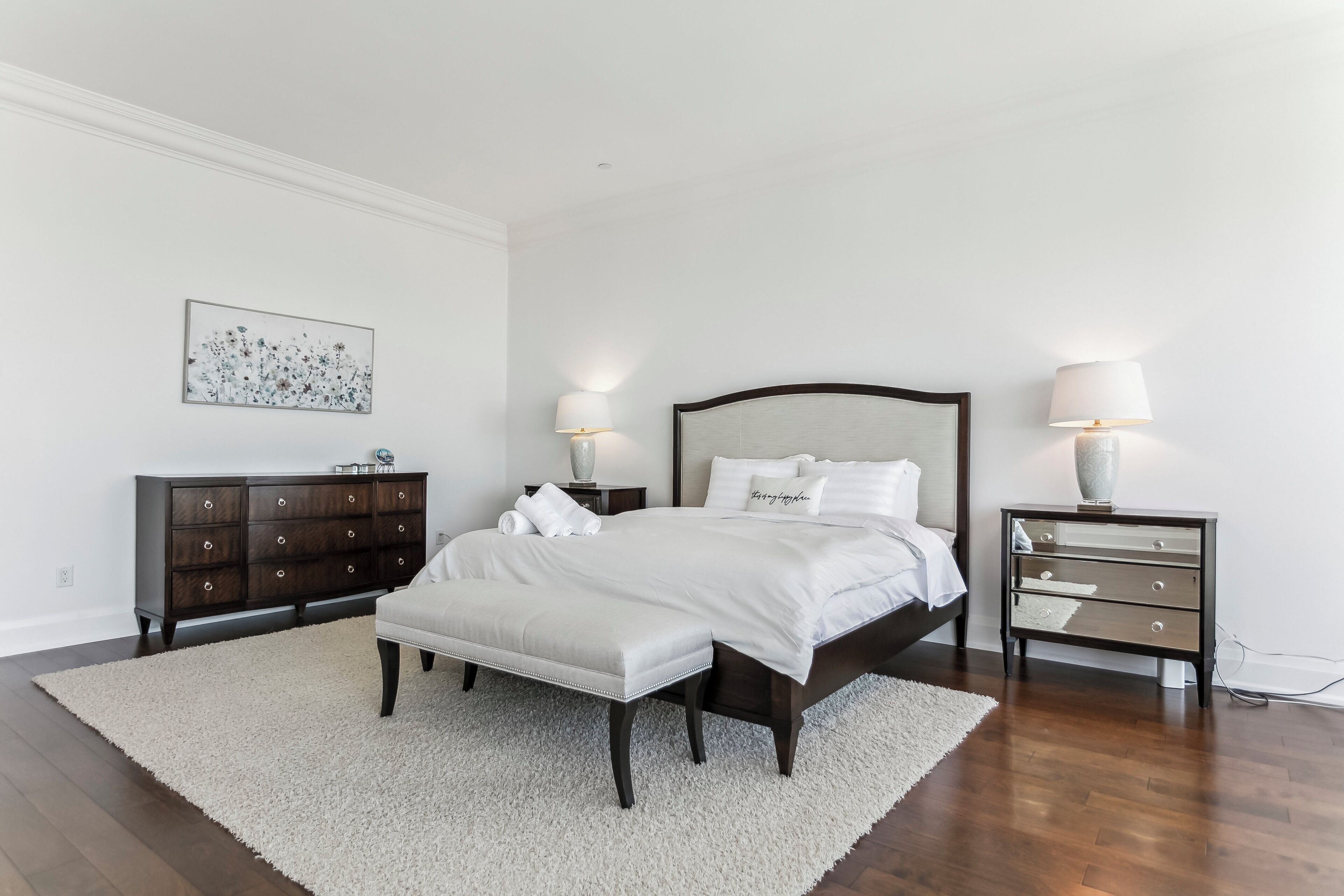 A bedroom with a large bed, two bedside tables, a dresser, and a rug.